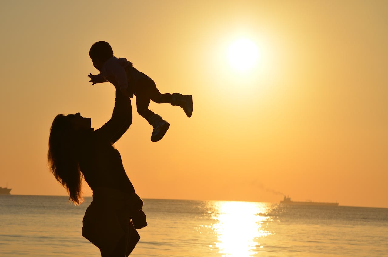 The Art of Drawing Readers In: Your attractive post title goes here Silhouette of a mother lifting her child at a sunset beach, capturing warmth and love.